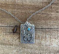 Spruce up your look with this adorable desert scene pendant. It is perfect for any age and can be bought as a pendant only or as a necklace. It is sterling silver, and has a cute little 3mm turquoise stone to complete the scene. This pendant measures 3/4" wide by 1" long. **No two stones are the same and you will NOT receive the stone pictured, however you can let us know your turquoise color preference (more green, bluer) in the notes section and we will try to accommodate you.** Solid Sterling Silver Jewelry, Handmade in Texas by artist Shandon Camarillo-Whitson Engraved Silver Turquoise Necklace In Southwestern Style, Southwestern Turquoise Pendant Necklace Stamped 925, Scene Necklace, Southwestern Silver Turquoise Inlay Necklace, Arid Landscape, Nickel-free Silver Southwestern Necklace, Desert Scene, Western-style Sterling Silver Turquoise Pendant Necklace, Faith Jewelry