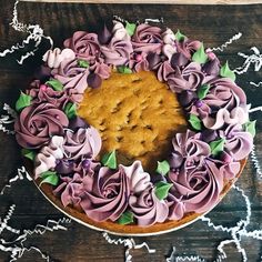 a cake decorated with pink and purple icing on a wooden table next to white doily