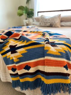 a crocheted blanket sitting on top of a bed next to pillows and blankets