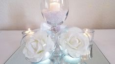 two white roses are sitting on a glass table with candles in the center and some lights around them