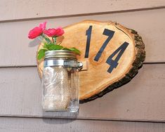 a mason jar with flowers in it hanging on the side of a house number sign