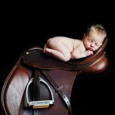 a baby laying on top of a brown saddle