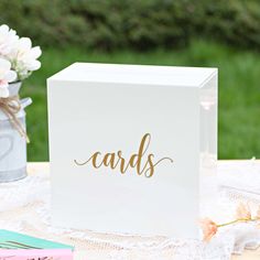 a white card box sitting on top of a table next to flowers and other items