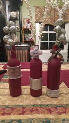 three red wine bottles are sitting on a table with silver balls in the middle and ribbons tied to them