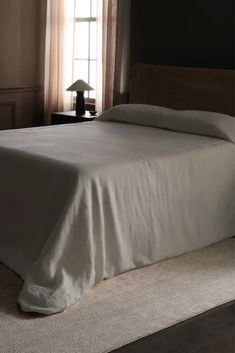 a bed with white sheets and pillows in a bedroom next to a lamp on a table