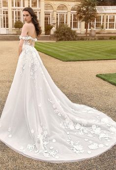 a woman in a white wedding dress standing on a driveway with her back to the camera