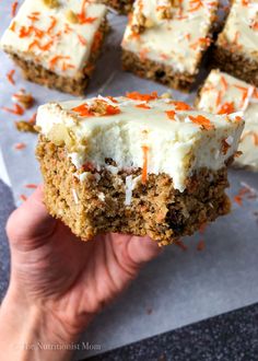 someone holding up a piece of carrot cake with white frosting and orange sprinkles