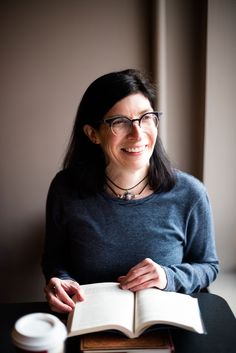 a woman sitting at a table with an open book in front of her, smiling