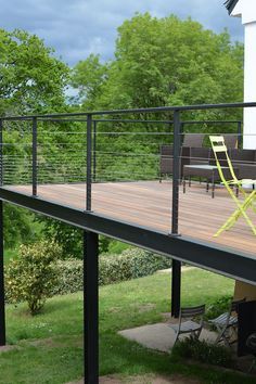 a deck with chairs and table on it in front of some trees, grass and bushes