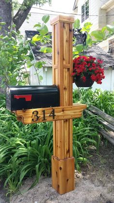 a wooden post with a mailbox attached to it in front of some plants and flowers