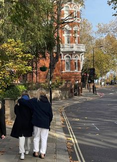 two women walking down the sidewalk in front of a tall brick building with a clock tower