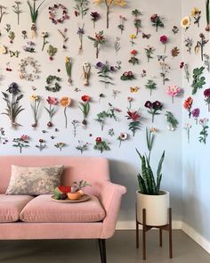 a pink couch sitting in front of a white wall covered in fake flowers and plants