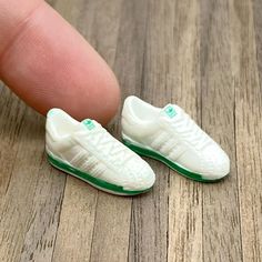 a tiny white shoe with green trim on the toe is being held by a finger