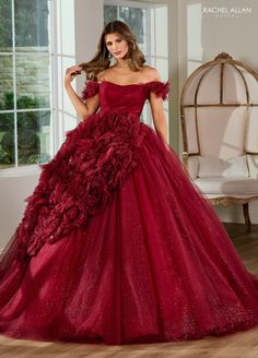 a woman wearing a red gown with flowers on the skirt and shoulder, standing in front of