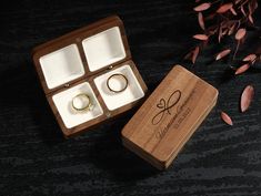 an open wooden box with two rings in it on a black surface next to dried flowers