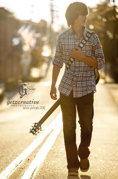 a young man is walking down the street with his guitar