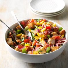 a white bowl filled with salad next to two plates on a wooden table and one has a fork in it