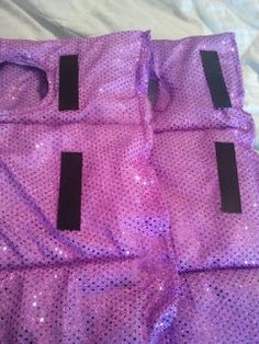 three purple bags sitting on top of a bed covered in sequins and black tags