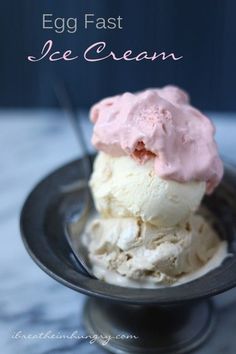 two scoops of ice cream sitting on top of a black plate with pink icing