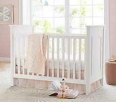 a white crib with a pink blanket and books on the floor next to it