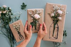 two hands holding wrapped gifts with flowers on them and wrapping them in brown paper, surrounded by greenery