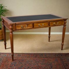 an antique desk with two drawers and a chalkboard top, in front of a potted plant