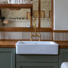 a kitchen sink sitting under a mirror next to a counter top with wine glasses on it