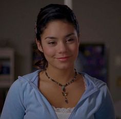 a woman wearing a blue shirt and necklace with beads on it's neck is looking at the camera