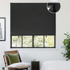 a living room with black roller shades on the windows and white walls, along with a brown chair