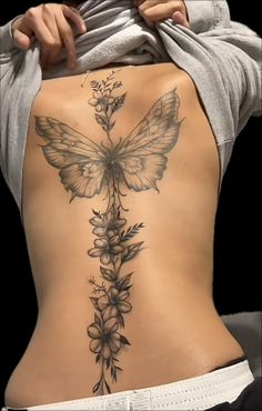 the back of a woman's body with flowers and a butterfly tattoo on it