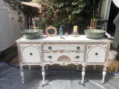 an old dresser with two bowls on top and one bowl at the bottom, sitting in front of a house