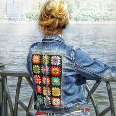 a woman wearing a jean jacket with colorful crochet on the back and sides