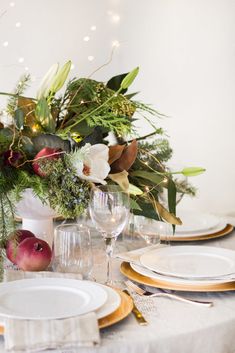 the table is set with white plates and gold rimmed glasses, silverware, greenery, and flowers