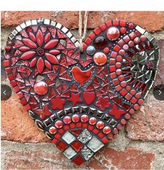 a red heart hanging on a brick wall with beads and glass mosaics in the shape of hearts