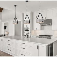 a large kitchen with white cabinets and stainless steel appliances, along with two pendant lights hanging from the ceiling