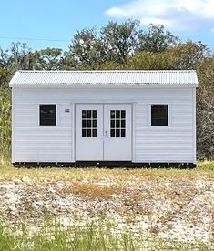 a small white building sitting in the middle of a field with tall grass and trees