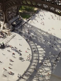 an aerial view of people walking around in the sun under a large metal structure with a long shadow on it