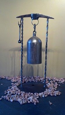 a metal bell sitting on top of a table next to some rocks and pebbles in front of a wall