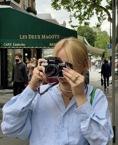 a woman taking a photo with her camera on the street in front of a cafe