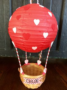 a red paper hot air balloon sitting on top of a wooden floor next to a basket