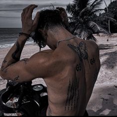 a man with tattoos on his back standing next to a motor bike at the beach