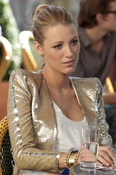 a woman sitting at a table with a glass in her hand and looking off to the side