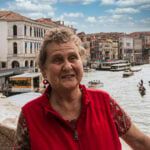 an older woman standing in front of a body of water with boats floating on it