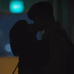 a man and woman kissing in front of a green traffic light at night with their arms around each other