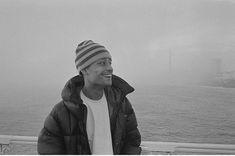 a man standing on top of a boat next to the ocean in front of a foggy sky