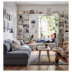 two people sitting in a living room with bookshelves and plants on the wall