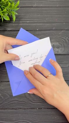 two hands holding an envelope with a handwritten message on it, next to a potted plant