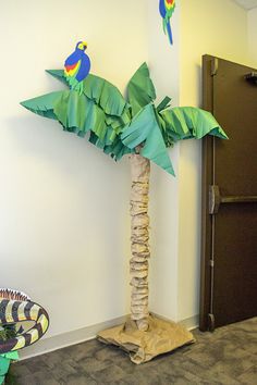 a palm tree made out of paper sitting in front of a wall with two parrots on it