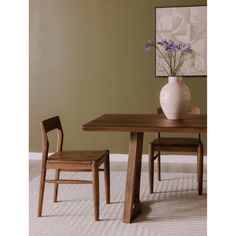 a wooden table with two chairs and a vase on top of it, in front of a green wall