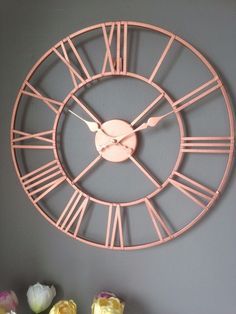 a large pink clock mounted to the side of a wall next to flowers and vases